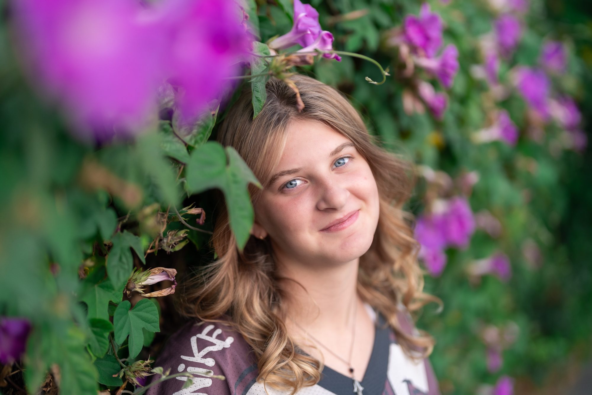 Close-up senior portrait among purple morning glory flowers, natural light