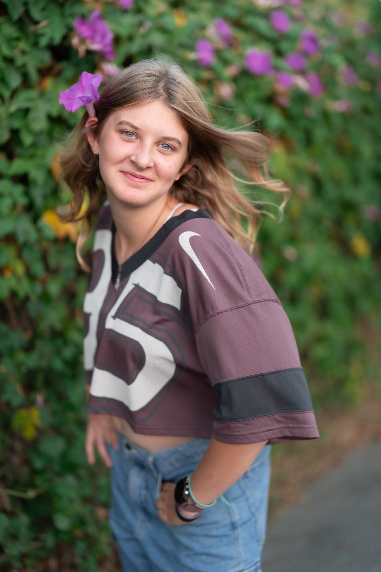 Senior in a maroon jersey with a flower in her hair, standing in a garden