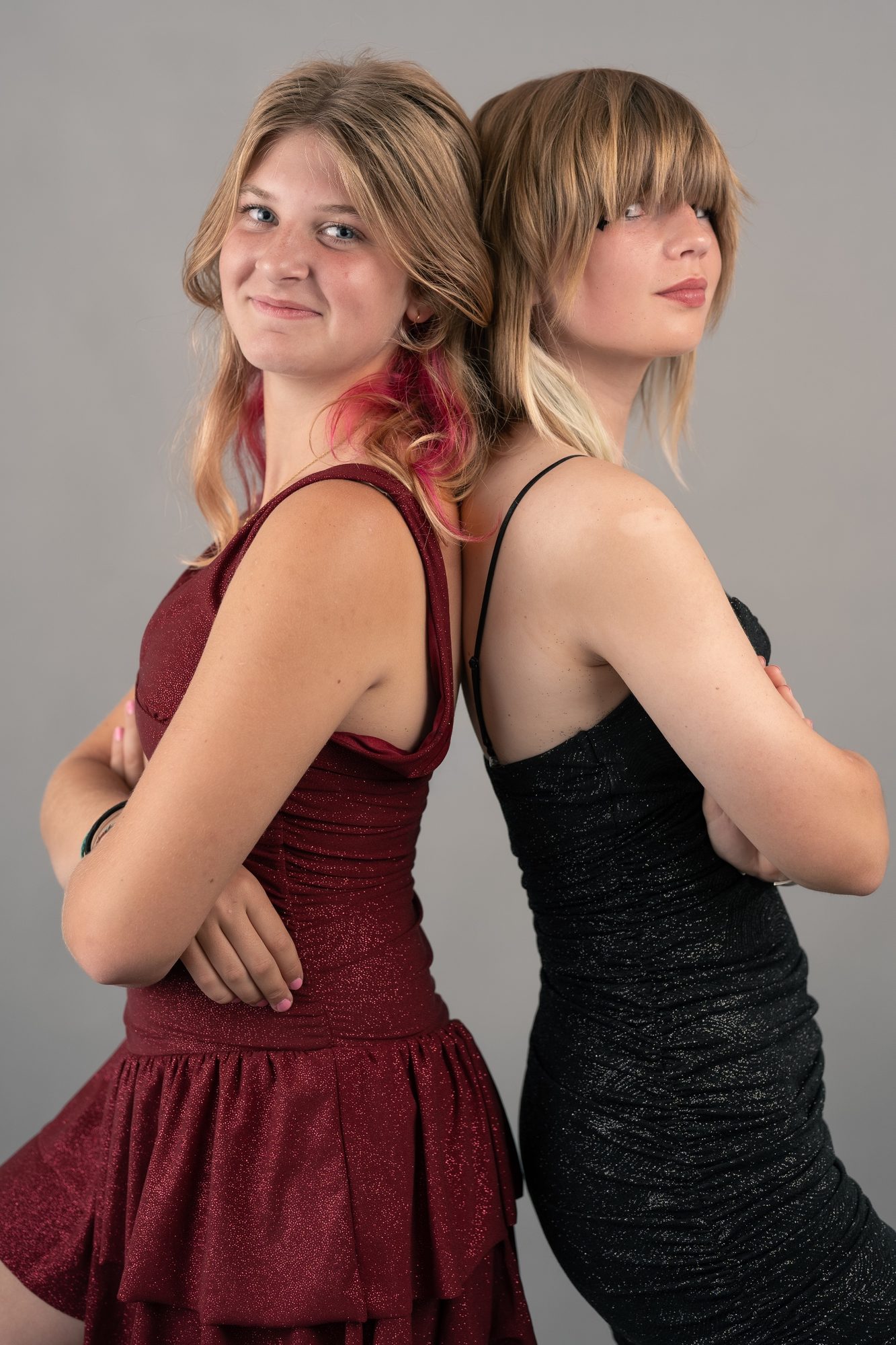 Two friends posing back-to-back in a studio, one in a burgundy dress and one in black