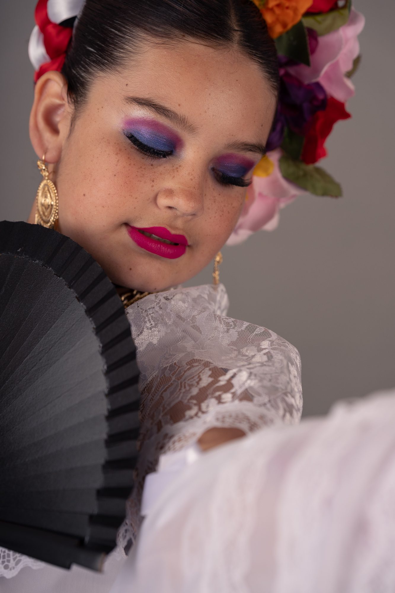 Close-up senior portrait in a colorful folklorico headdress and bold makeup, studio